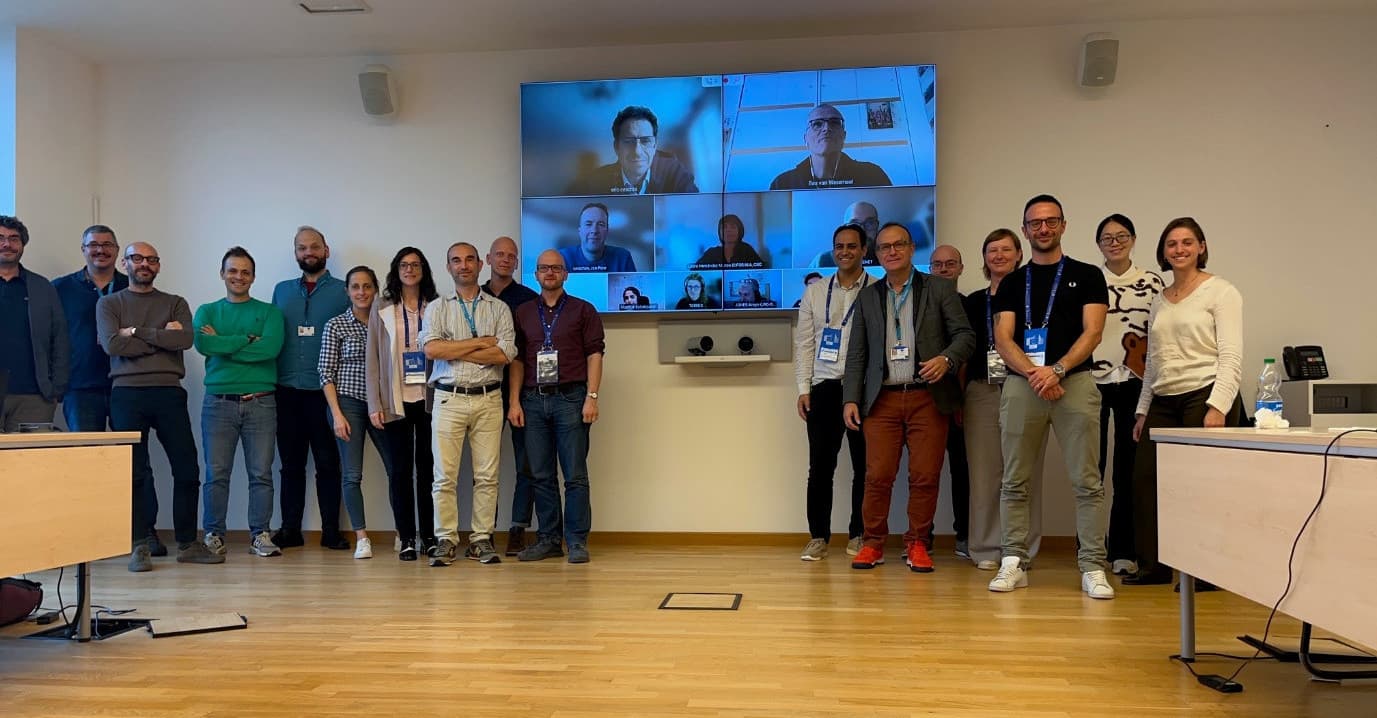 A diverse group of individuals gathered in front of a large screen, engaged in discussion or presentation.